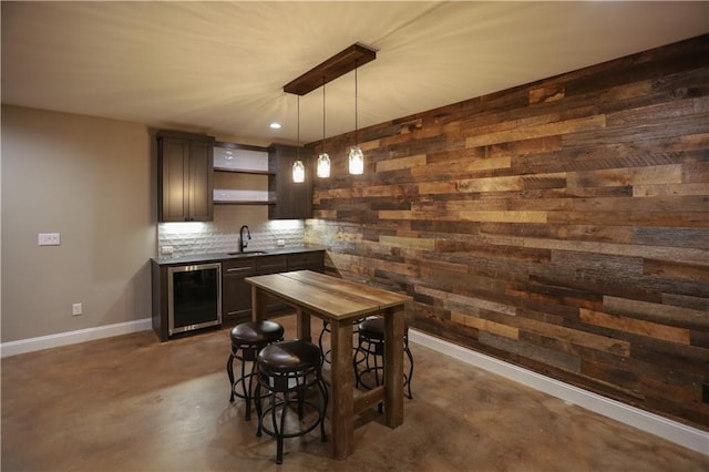 bar featuring wooden walls, sink, wine cooler, hanging light fixtures, and dark brown cabinets