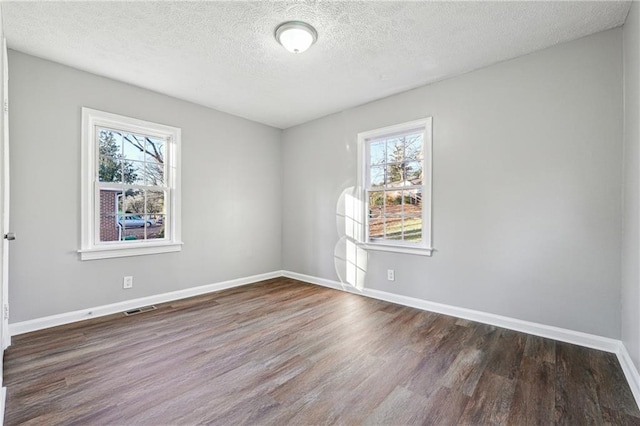 empty room featuring plenty of natural light, a textured ceiling, and dark hardwood / wood-style flooring