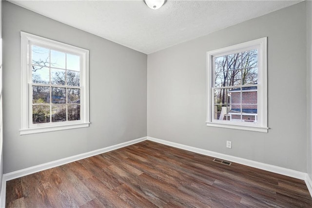 spare room featuring a textured ceiling, dark hardwood / wood-style flooring, and a healthy amount of sunlight