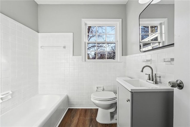 bathroom with hardwood / wood-style floors, vanity, tile walls, toilet, and a tub to relax in