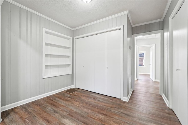 unfurnished bedroom featuring a textured ceiling, a closet, crown molding, and dark hardwood / wood-style floors