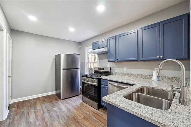 kitchen featuring sink, appliances with stainless steel finishes, blue cabinetry, dark hardwood / wood-style flooring, and light stone counters