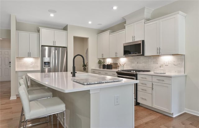 4297 Azalea Ridge Way, Hoschton, GA 30548 - kitchen with appliances with stainless steel finishes, an island with sink, light wood-style flooring, tasteful backsplash, and a kitchen bar