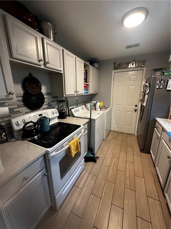 kitchen featuring stainless steel refrigerator, white electric stove, gray cabinetry, decorative backsplash, and washing machine and dryer