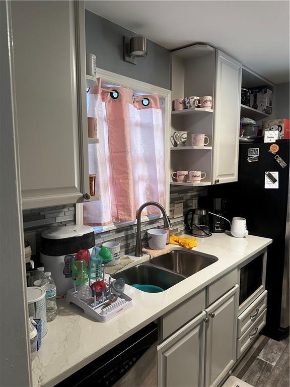 kitchen with dark wood-type flooring, sink, tasteful backsplash, black refrigerator, and stainless steel dishwasher