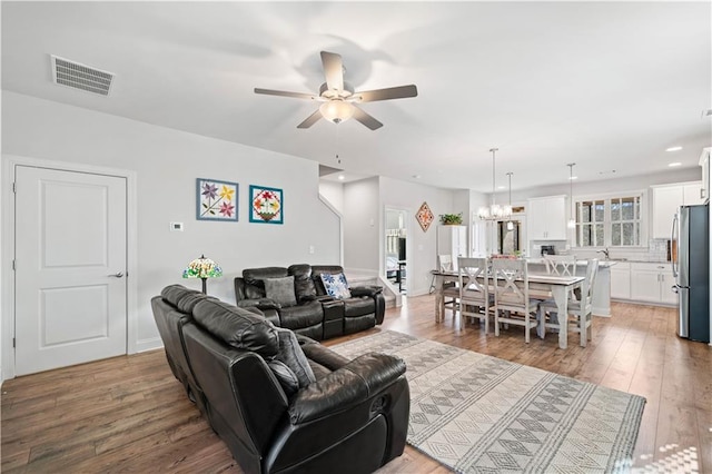 living area with recessed lighting, visible vents, light wood-style flooring, and ceiling fan with notable chandelier