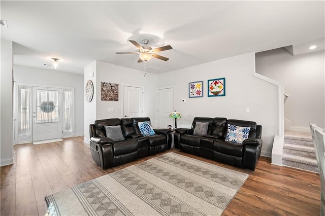 living area with a ceiling fan, stairway, baseboards, and wood finished floors