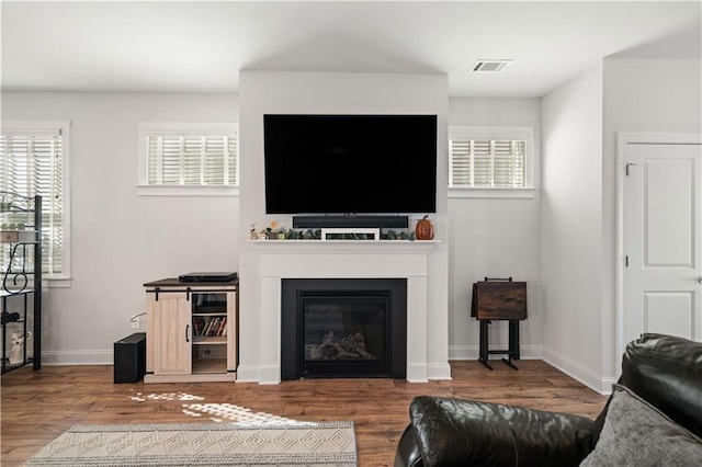 living area featuring a wealth of natural light, a fireplace, wood finished floors, and visible vents