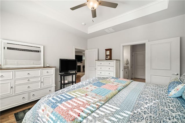 bedroom featuring dark wood-style floors, crown molding, a raised ceiling, visible vents, and ensuite bath