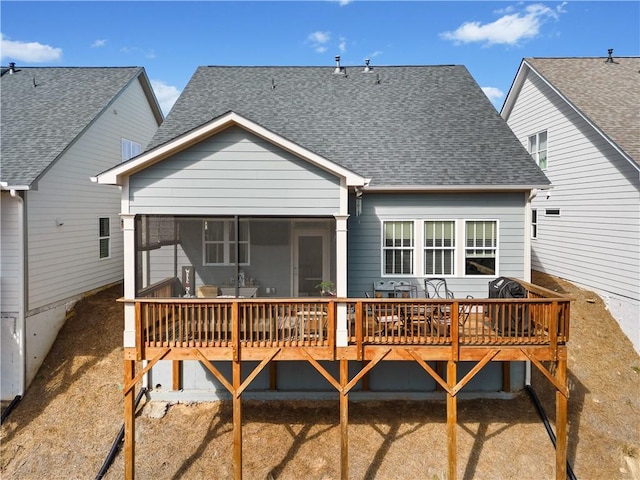 back of property with a shingled roof, a wooden deck, and a sunroom