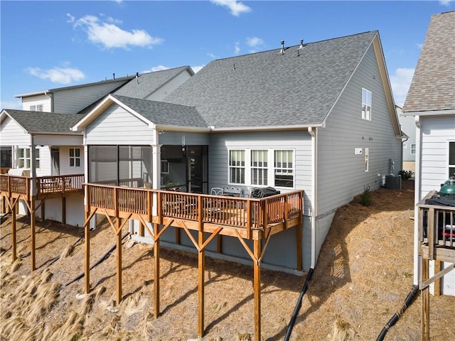 back of property with a sunroom, a wooden deck, cooling unit, and roof with shingles