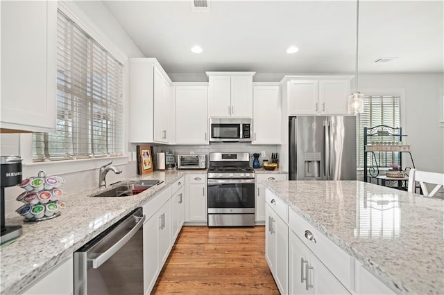 kitchen featuring light wood finished floors, backsplash, appliances with stainless steel finishes, white cabinets, and a sink