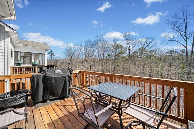 wooden deck with a forest view, a grill, and outdoor dining space