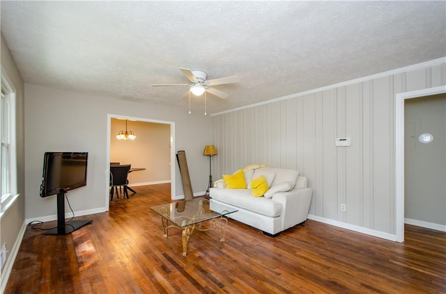 living room with a textured ceiling, ceiling fan with notable chandelier, crown molding, and dark wood-type flooring