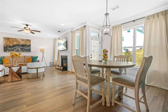 dining room featuring a glass covered fireplace, visible vents, and light wood-style flooring