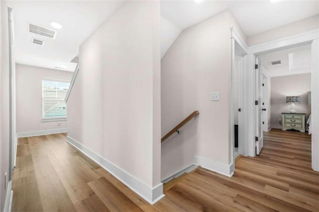 corridor with wood finished floors, visible vents, baseboards, and an upstairs landing