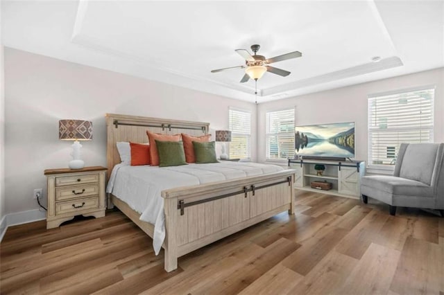 bedroom with baseboards, a ceiling fan, a tray ceiling, and light wood-type flooring
