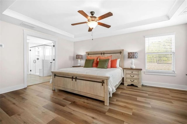 bedroom with a raised ceiling, visible vents, connected bathroom, baseboards, and light wood-style flooring