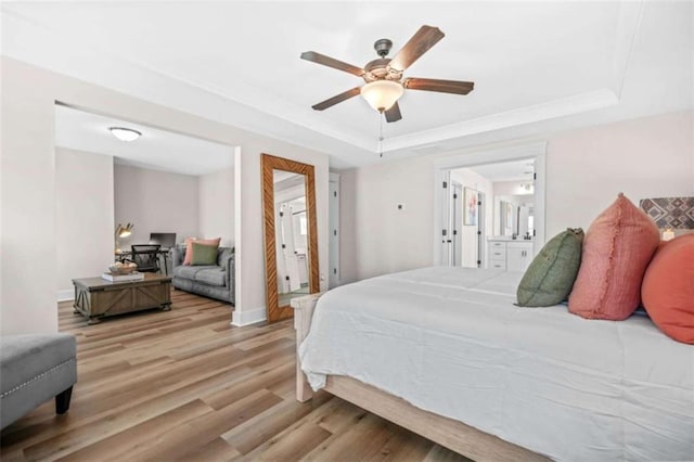 bedroom with a raised ceiling, wood finished floors, ensuite bath, and ceiling fan