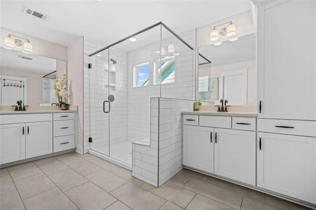 bathroom featuring a shower stall, tile patterned floors, visible vents, a sink, and two vanities
