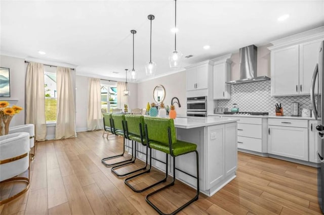 kitchen featuring light countertops, a breakfast bar, wall chimney exhaust hood, a kitchen island with sink, and tasteful backsplash