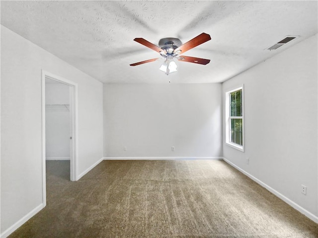 empty room with a textured ceiling, dark carpet, and ceiling fan