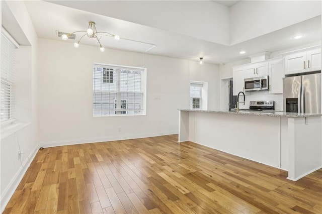 kitchen with appliances with stainless steel finishes, white cabinetry, backsplash, light stone counters, and light wood-type flooring