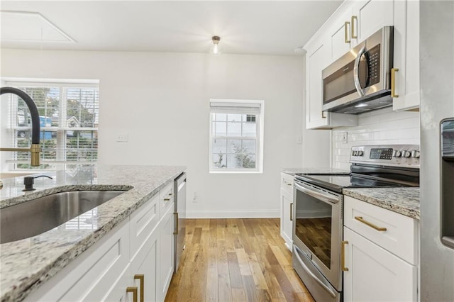 kitchen with sink, appliances with stainless steel finishes, tasteful backsplash, light stone countertops, and white cabinets