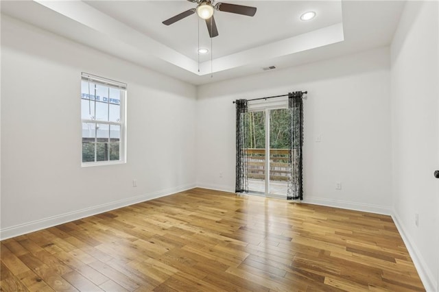 spare room with ceiling fan, plenty of natural light, a tray ceiling, and light wood-type flooring