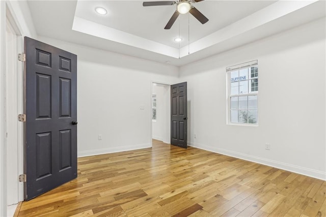 spare room featuring light hardwood / wood-style flooring, ceiling fan, and a tray ceiling