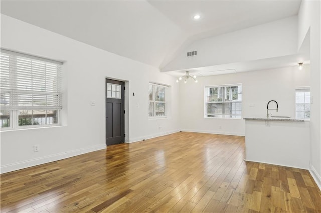 unfurnished living room with hardwood / wood-style flooring, high vaulted ceiling, a chandelier, and sink