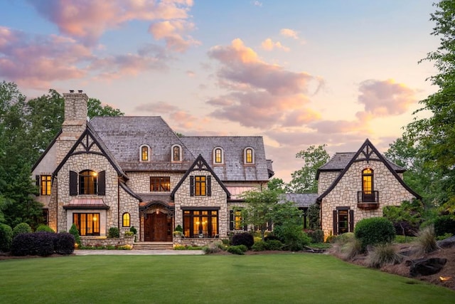 french country home with a chimney, a yard, and stone siding