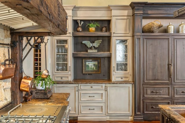 interior space featuring stove, dark brown cabinets, glass insert cabinets, dark stone counters, and cream cabinetry