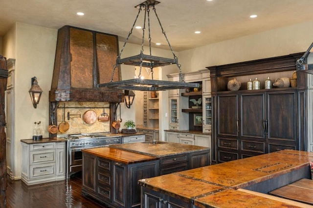 kitchen featuring double oven range, open shelves, a center island with sink, butcher block counters, and recessed lighting
