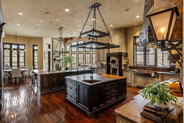 kitchen featuring an island with sink, recessed lighting, a sink, dark wood finished floors, and decorative light fixtures