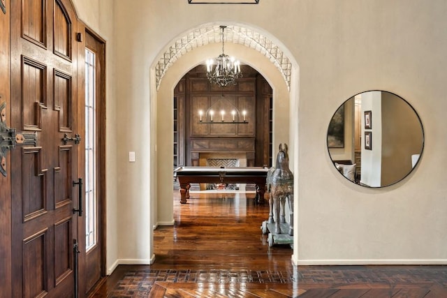 entryway featuring an inviting chandelier, arched walkways, baseboards, and dark wood finished floors