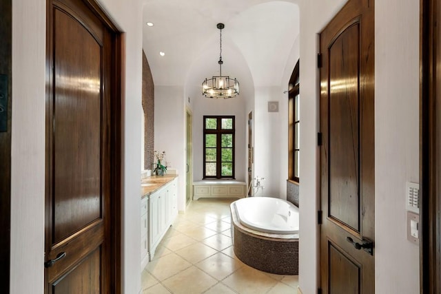 bathroom with an inviting chandelier, vanity, tile patterned floors, a bathtub, and vaulted ceiling