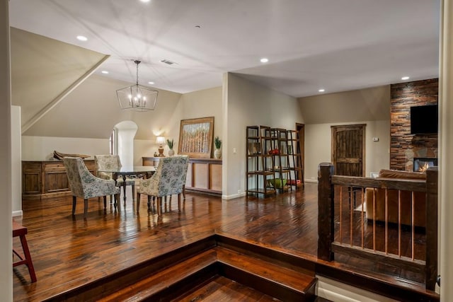 dining area featuring wood-type flooring, a notable chandelier, lofted ceiling, and a fireplace