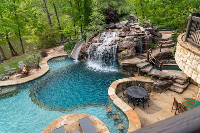 outdoor pool with a patio, a wooded view, and an outdoor fire pit