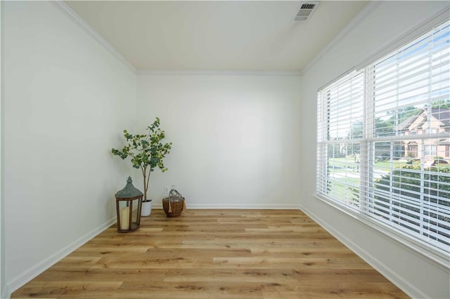 empty room with light wood-style floors, baseboards, visible vents, and crown molding