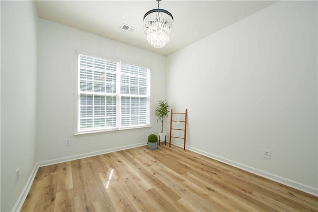 spare room featuring baseboards, visible vents, a chandelier, and wood finished floors