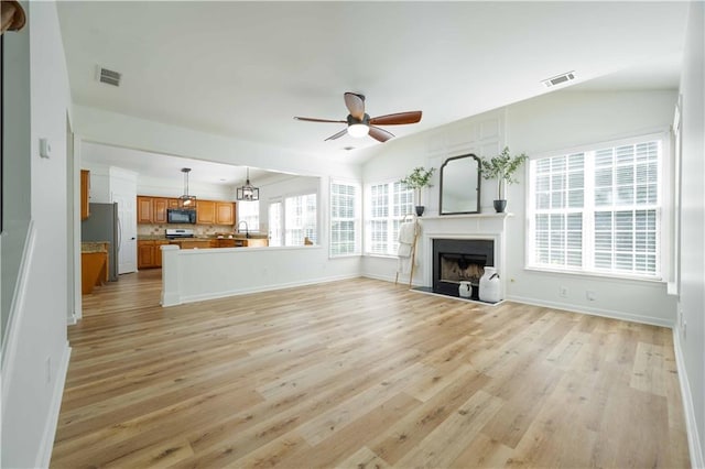 unfurnished living room with a ceiling fan, light wood-style floors, visible vents, and a fireplace