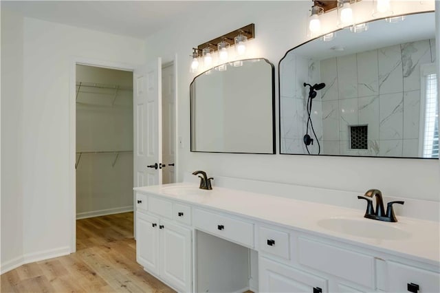 full bath with tiled shower, a sink, a spacious closet, and wood finished floors