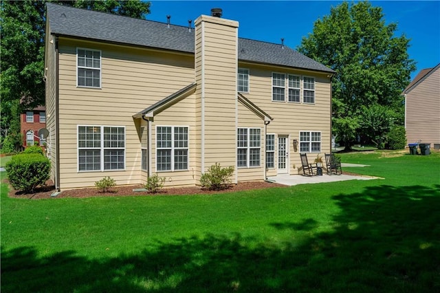 back of house with a yard, a shingled roof, a chimney, and a patio