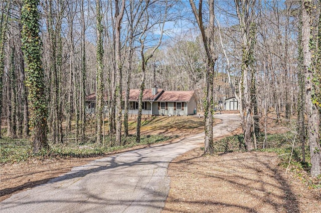 view of front of home featuring aphalt driveway, a porch, a wooded view, and a chimney