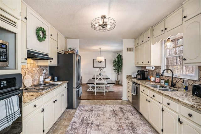 kitchen with tasteful backsplash, under cabinet range hood, stainless steel appliances, a textured ceiling, and a sink