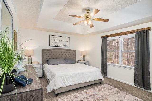 carpeted bedroom featuring baseboards, a textured ceiling, a tray ceiling, and a ceiling fan