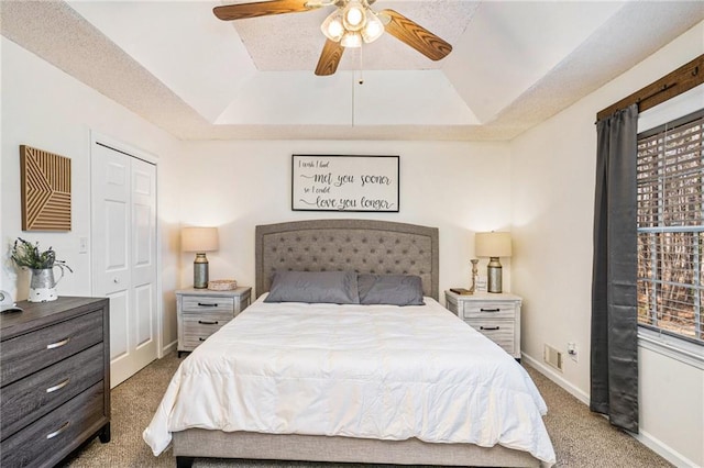 carpeted bedroom with a raised ceiling, a ceiling fan, baseboards, and a closet