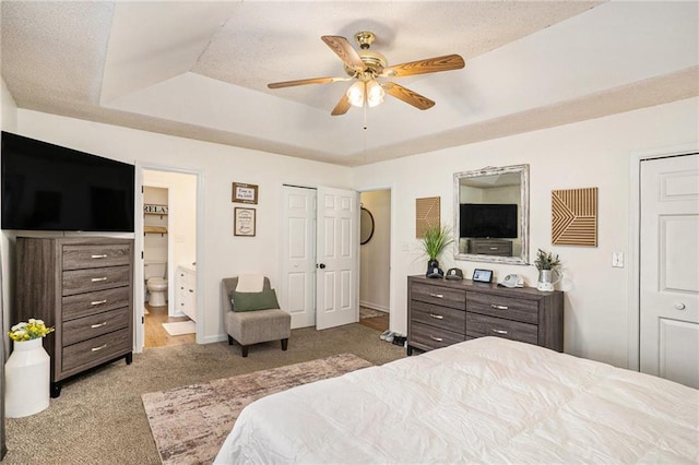 carpeted bedroom featuring a ceiling fan, baseboards, ensuite bathroom, a textured ceiling, and a raised ceiling