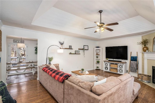 living area featuring a fireplace with flush hearth, a ceiling fan, hardwood / wood-style flooring, crown molding, and a raised ceiling